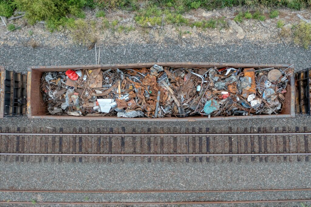 Aerial shot of an open railcar loaded with assorted scrap metal on train tracks.